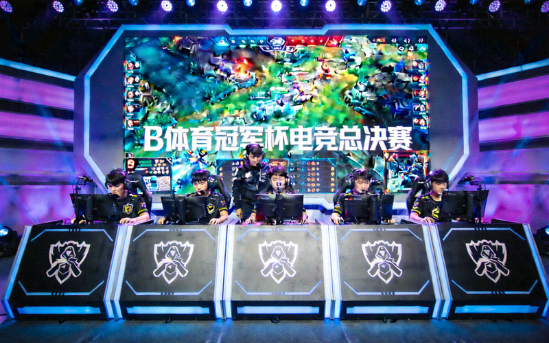 B体育冠军杯电竞总决赛：涅槃战队与巅峰战队在舞台上全神贯注操作，背后大屏幕显示游戏战况